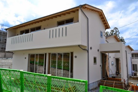 白い外壁と木の屋根を持つ二階建ての戸建て住宅が完成間近で、入口やベランダの様子が見える戸建て災害公営住宅の写真