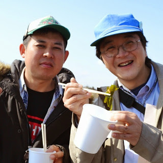 紙コップの汁物を食べ終わった男性2名が笑顔で写っている写真