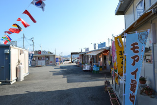 青空の下、万国旗やのぼりが風になびく、様々な店舗が並ぶ商店街の写真