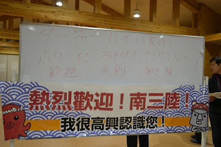 ホワイトボードに中国語とその読み方のカタカナが書かれており、その下に波のデザインにタコなどのイラストが描かれ、歓迎の言葉が中国語で書かれた横断幕が貼られている写真