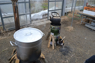 ハウスの中で、まきがくべられた上に置かれた大きな蓋つきの寸胴鍋が置かれ、その横のストーブには蒸気をあげたヤカンが置かれている写真