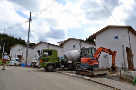 新しく建設中の戸建て住宅が道路沿いに立ち並び、屋外でコンクリートミキサー車や重機が作業をしている、戸建て災害公営住宅の建設現場の写真