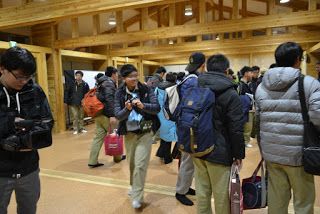 到着した学生たちが大きな荷物を持って続々と会場に集まっている様子の写真