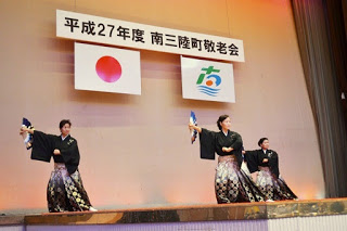 舞台上で三人の女性が黒い着物姿で扇子を持ち、見事な踊りを披露している場面の写真