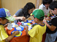 子どもたちがテーブルの周りに集まり、青い皿に乗ったたくさんのダンゴウオカードに見入っている写真