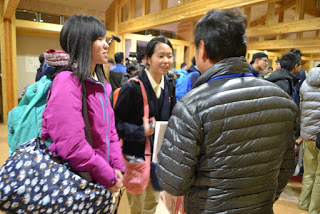 たくさんの荷物を持った女子学生二人が笑顔で男性と向かい合っている写真