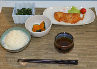 白ご飯、カボチャの料理、青野菜の料理、レタスとミニトマトが添えられた揚げ物の料理がそれぞれ器に盛りつけられて並び、お茶と箸が添えられている写真