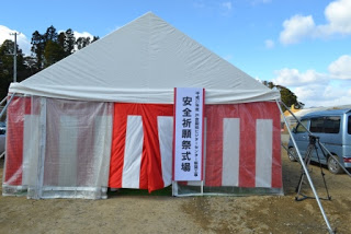 白い屋根のテントの周りを囲んで紅白幕が取り付けられ、その前に「安全祈願祭式場」の看板が設置された会場の外観写真