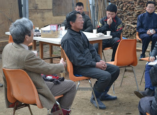 白いテーブルの前や横に置かれたオレンジ色の椅子に座った男性たちが会話をしている様子の写真