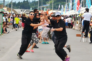 黒い服を着たグループが2人ずつ向かい合い手を交差させながら、笑顔で元気よく踊っている様子の写真
