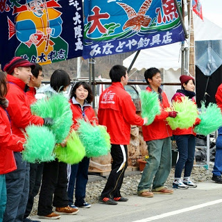 赤いジャンバーを着たスタッフの人たちが緑のボンボンをもって整列している写真