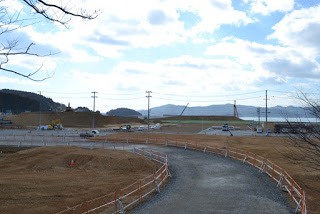 広い駐車場へ続く細い道の左右に土が盛られている様子の写真