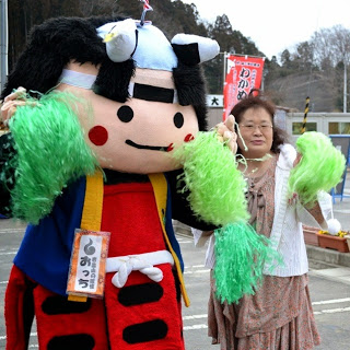 緑のボンボンを持った岩出山おっちくんと女性が記念撮影をしている写真