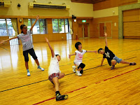 3人の女の子が床に座ったり片手をついたりしたポーズをとり、後ろでもう一人の女の子が立って腕を広げたポーズをとっている写真