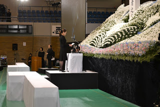 ステージ前に置かれた白いクロスが掛けられた演台に立ち、慰霊碑に向かって手紙を読む女性の写真