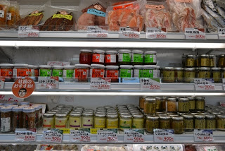 値札が付いている冷蔵棚に、瓶詰の調味料やパック詰の切り身などがずらりと並んでいる写真