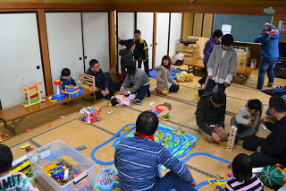 和室の室内に子どもと大人が集まり、おもちゃや電車セット、レゴなどで自由遊びを楽しんでいる地域交流の様子の写真