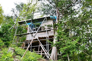 木々に囲まれた山の斜面に建てられた小屋に足場が組まれており、工事中の様子がうかがえる写真