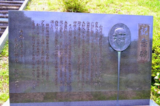 黒い石碑に長い日本語の文章と人の横顔のレリーフが彫られている記念碑の写真