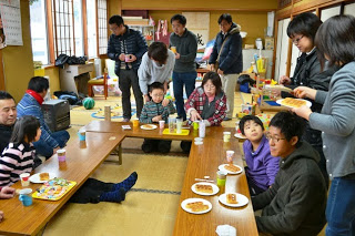 子どもたちと大人が長机を囲んでお菓子や飲みものを楽しみながら会話している交流の様子の写真