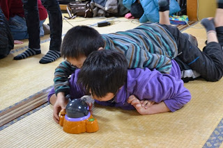 二人の男の子が床に寝そべって、アニメのキャラクターのおもちゃでじゃれあって遊んでいる様子の写真