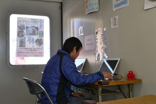 コンテナの中で、猪又隆弘センター長が机の前に座り、ノートパソコンを操作している様子の写真