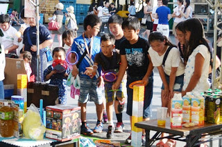 屋外のブースで、子どもたちが飲み物やお菓子などの景品を狙い輪投げを行っている様子の写真