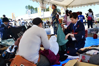 青いシートの上で着物を手に取って品定めをする女性たちと、それを手伝う着物姿のスタッフが写っている写真