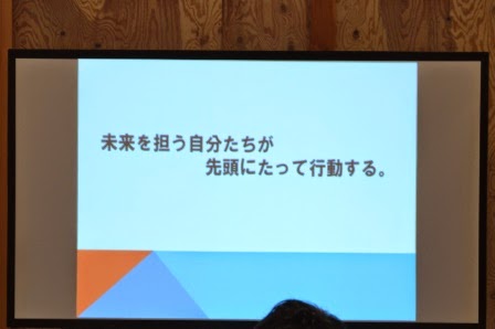 木目の壁に囲まれた室内で、「未来を担う自分たちが先頭にたって行動する。」という力強いメッセージがスクリーンに映されている様子をアップで撮影した写真