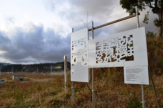 草が茂る空き地の一角に白い切り絵アートのボードが金属の枠に取り付けられ展示されている様子の写真