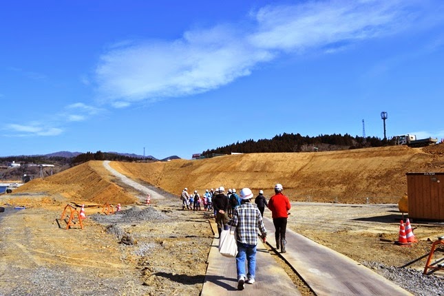 ヘルメットをかぶった見学者の一団が造成地の中を歩いており、左右には土が盛られた場所や工事資材が見える、現場内を歩いて見学している写真