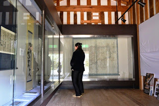 部屋の奥と左側にガラス張りの展示品が並べられ女性が見ている写真