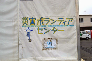 青と黄色の文字で書かれた「災害ボランティアセンター」の表示が白いテントの外側、側面に貼られている写真