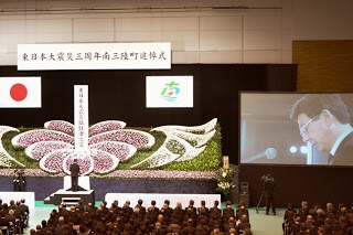 右側の大きなスクリーンに佐藤仁町長が映し出され、祭壇と向かい合わせになるように設置されたマイクで佐藤仁町長が式辞を述べている写真