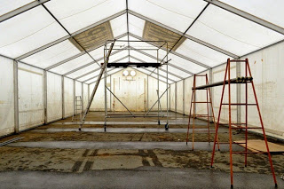 2つの赤い脚立に鉄パイプが置かれ、中央に銀色の足場が組まれた白い大型テントの内部の写真