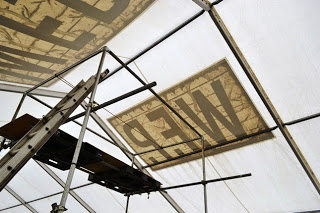 白いテントの内側から見上げた天井部分、外側に貼られた「W.F.P.」の文字がさかさまに透けて見えており、天井付近に足場の一部が写っている写真