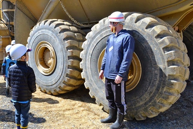 大きな建設用ダンプトラックのタイヤの前に大人が立っており、タイヤの大きさを実感できるように説明している様子の写真