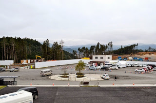 敷地の左側が空き地になっており、その隣に2階建ての建物、駐車場があり、手前に円形のロータリーがある様子を高い場所から撮影した写真