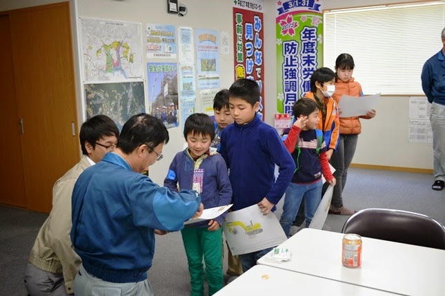 子供たちが描いた絵を手に持ちながら順番に並び、関係者に作品を見せている様子の写真