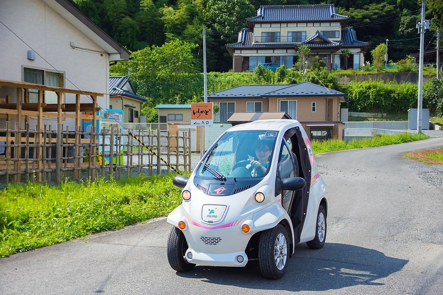 ハンドルを両手で握る女性が前方を見据えて運転席に座り小型電気自動車を運転している様子の写真