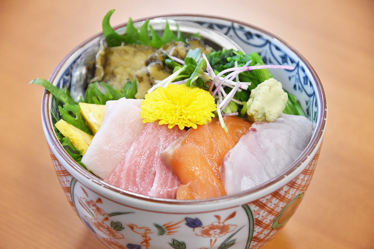 魚の刺身や貝が盛り付けられ、薬味や菊の花が飾られた海鮮丼の写真