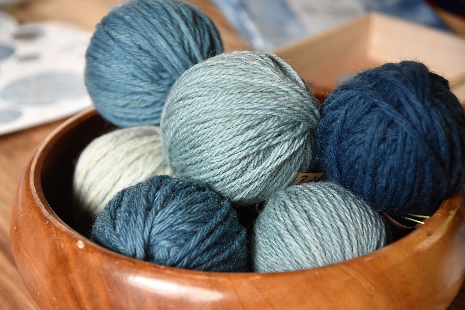 藍色に染まった濃淡の毛糸が数個、茶色の丸い入れ物に入っている写真