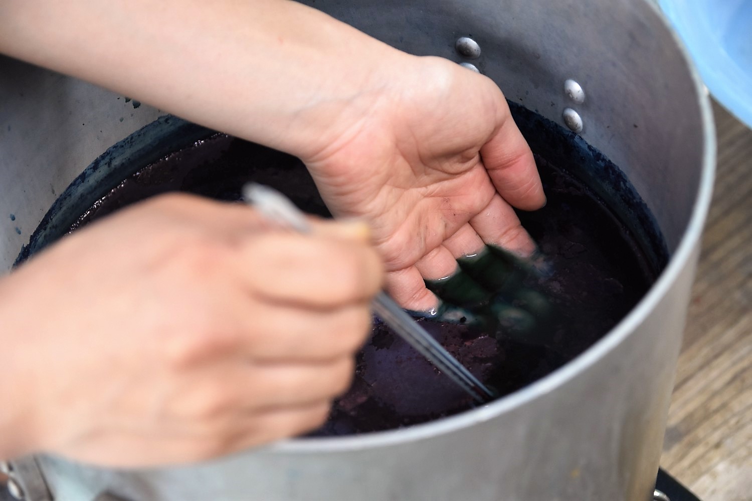 藍の葉を寸胴鍋で煮出して作った染料液の中に手を入れ温度を測っている写真