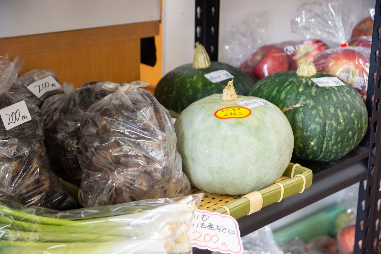 新鮮なかぼちゃや透明袋に入ったリンゴに里芋などの野菜や果物が陳列されている写真