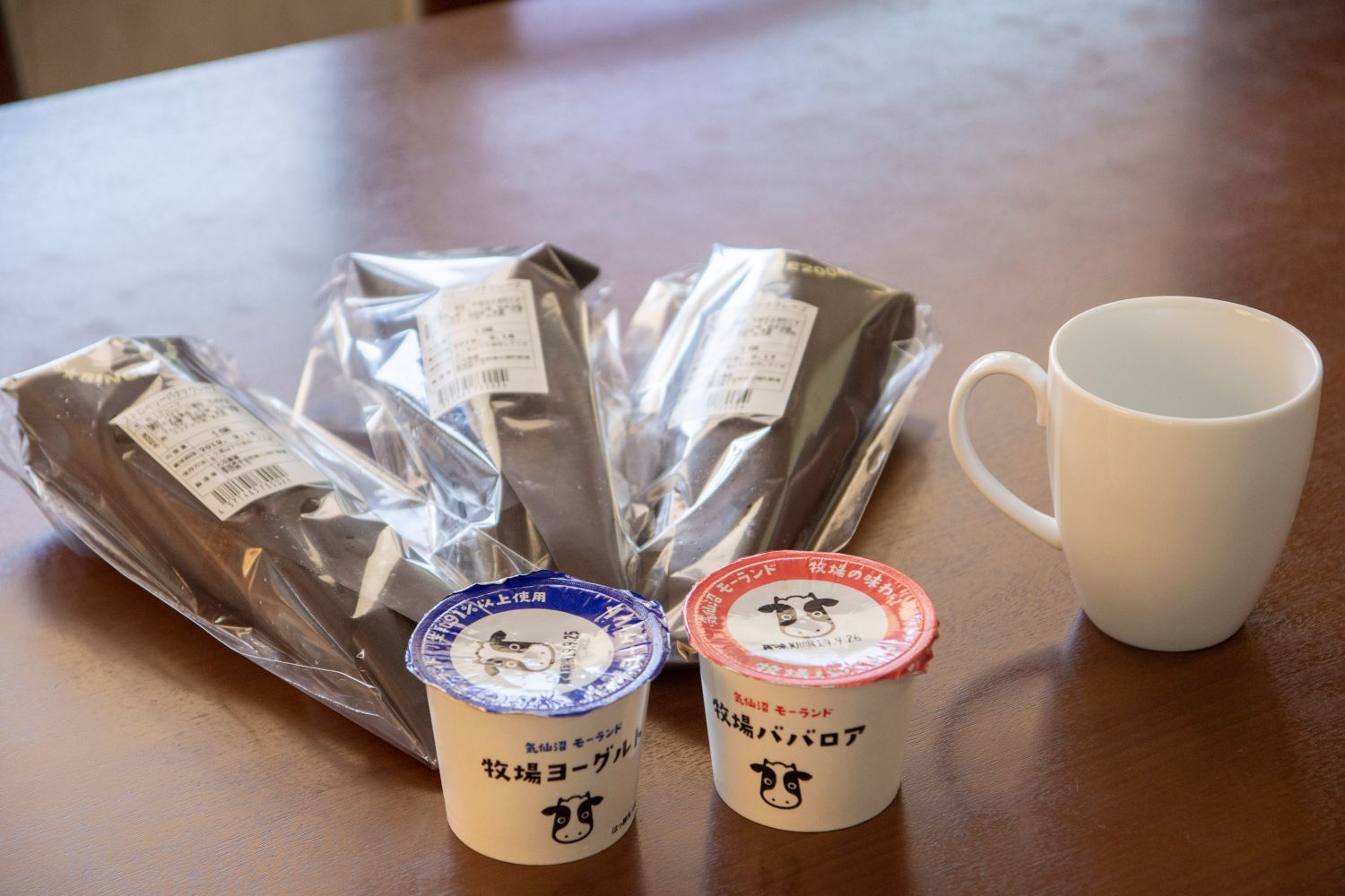 青と赤色の蓋がついた牧場ババロア、茶色の紙に包まれた透明の袋に入ったスイーツが並んでいる写真