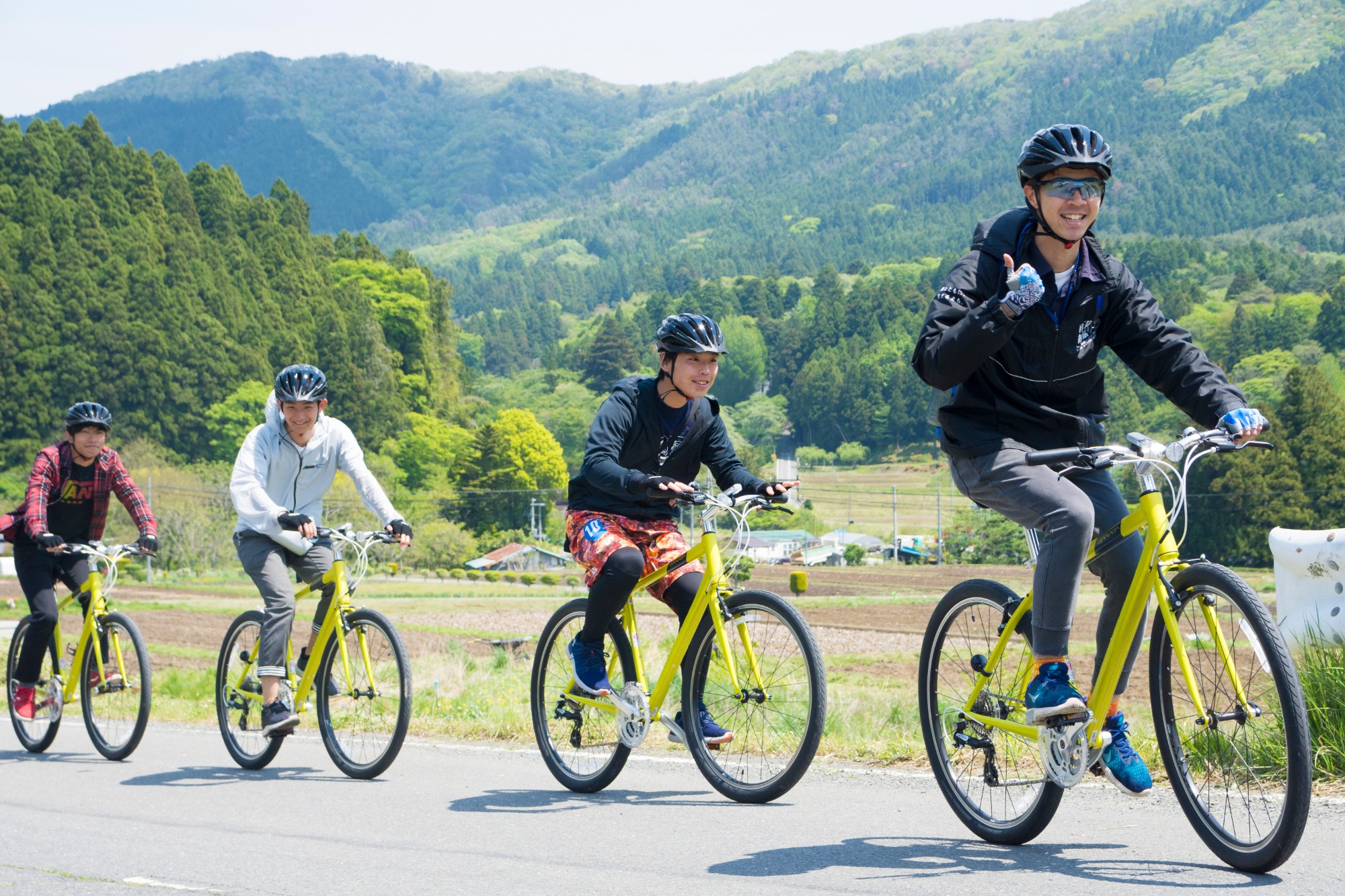 黒色のヘルメットを被りお揃いの黄色の自転車を漕いでいる4人の方々が入谷コースを縦一列に並んで走行している写真