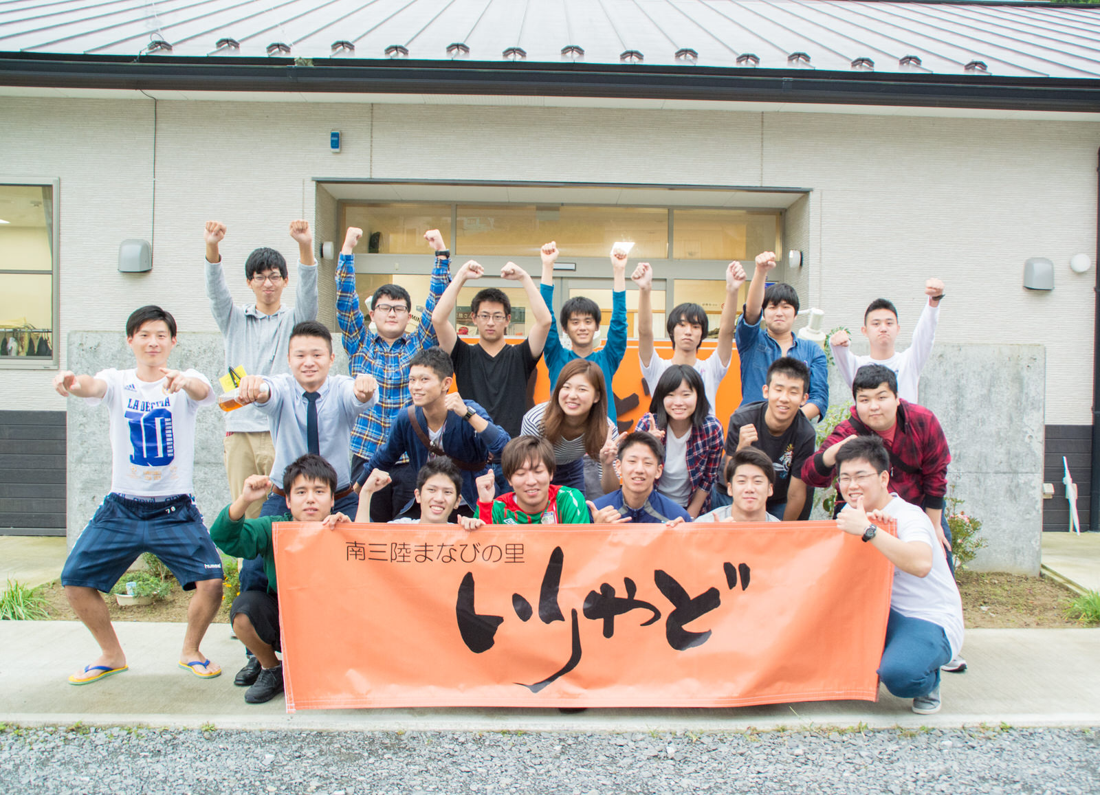たくさんの学生たちが建物の前で「南三陸まなびの里いりやど」と書かれたオレンジ色の横断幕を掲げながら元気にポーズを取っている集合写真