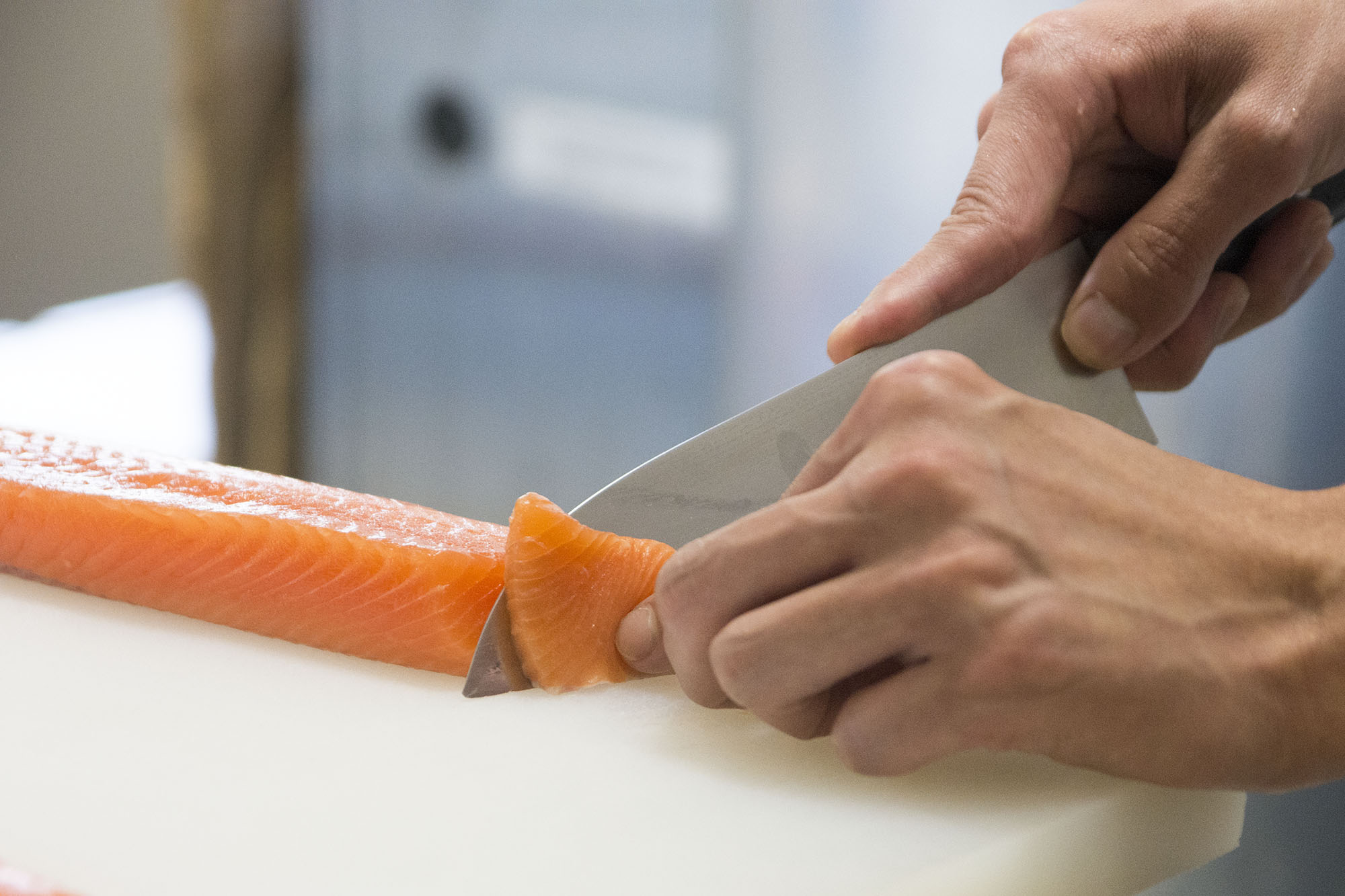 包丁で新鮮なサーモンの切り身を薄く丁寧にスライスしている手元をアップで撮影した写真