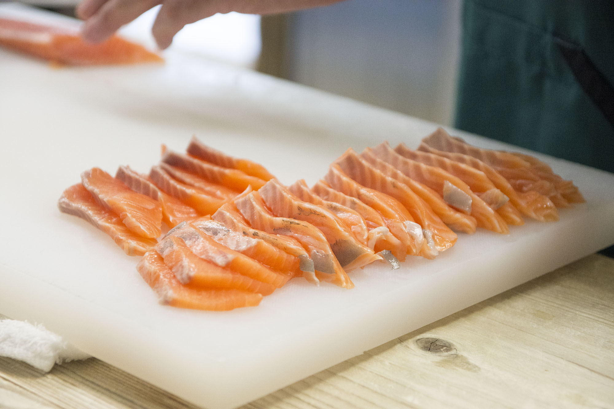 包丁を使って薄く鮭を切っている様子が写っており、手前に切った後の鮭の切り身がまな板の上に並んでいる写真