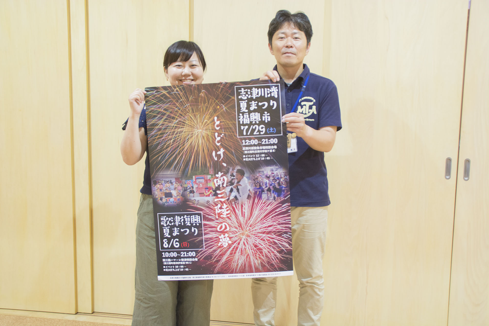 薄い木目調の室内の壁の前で、リポーターの女性と紺色のポロシャツを着た男性が並んで立ち、一緒に夏まつりのポスターを持っている写真